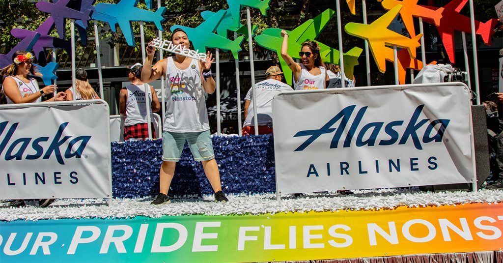 An Alaska Airlines float at a pride parade decorated with rainbow colored plans and the slogan "Our Pride Flies Nonstop."