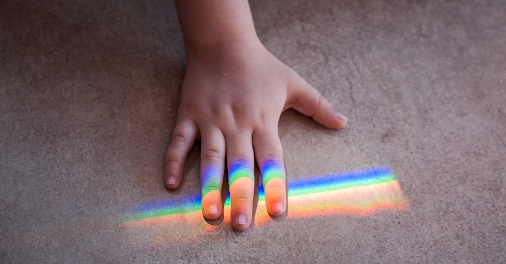 A child’s hand on the floor with a rainbow band of light across the fingers