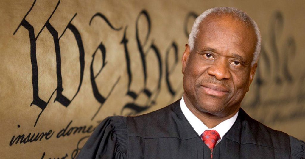 Justice Clarence Thomas in judicial robe before a blurred image of the U.S. Constitution, representing his originalist legacy on the Supreme Court.