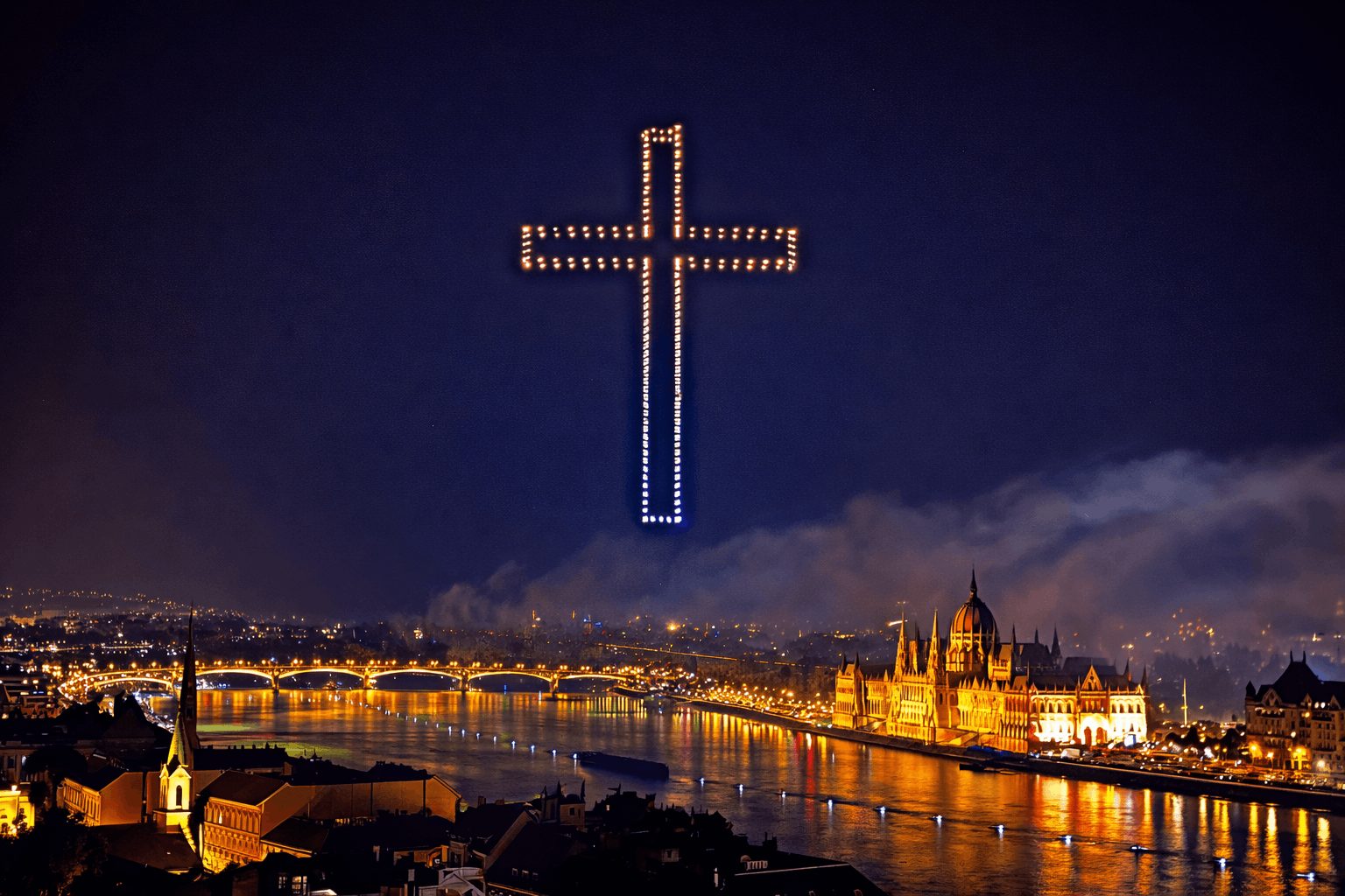 Illuminated cross formed by drones hovers above the Budapest city skyline at nighttime, with a river and historic buildings glowing below.