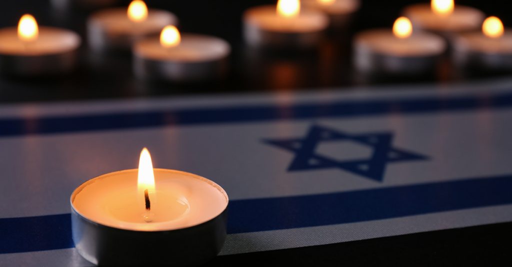 Lit tea-light candles on an Israeli flag, with more candles blurred in the background.