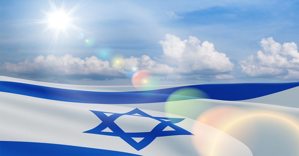 Israeli flag waving under a bright sun and blue sky with light flare.
