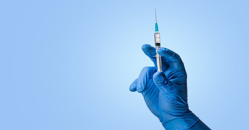 Blue-gloved hand holding a syringe against a light blue background.