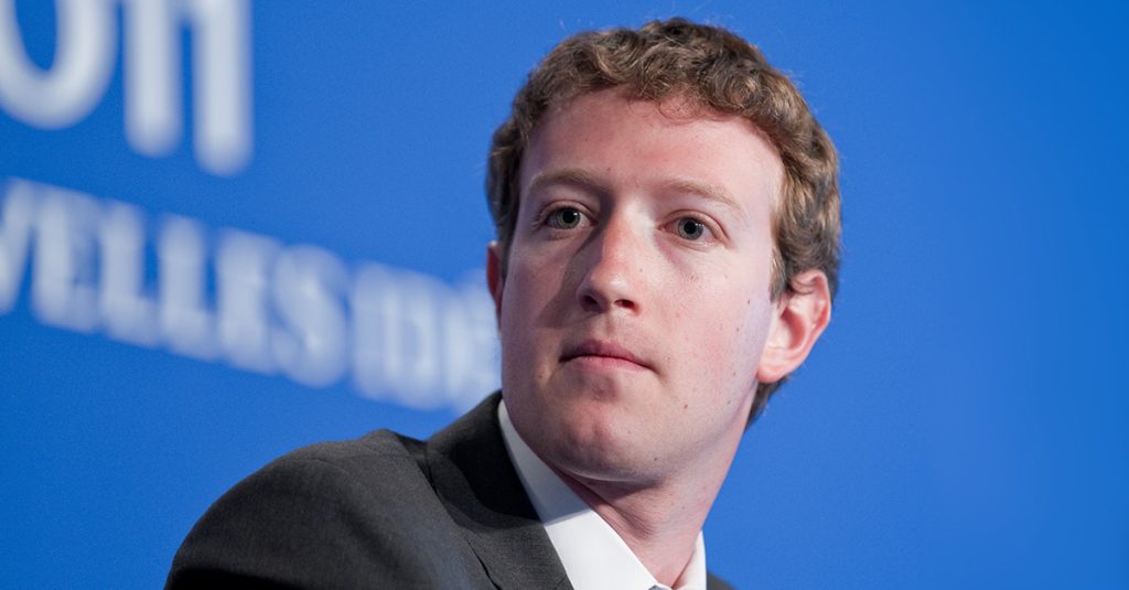 Mark Zuckerberg sits onstage in front of a blue conference backdrop.