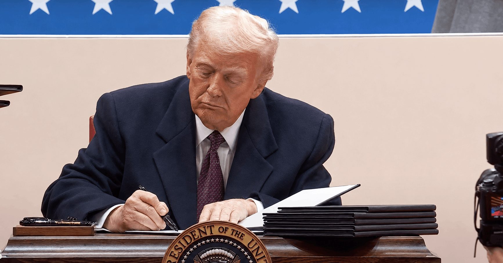 President Trump signs a stack of documents at a formal presidential signing event.