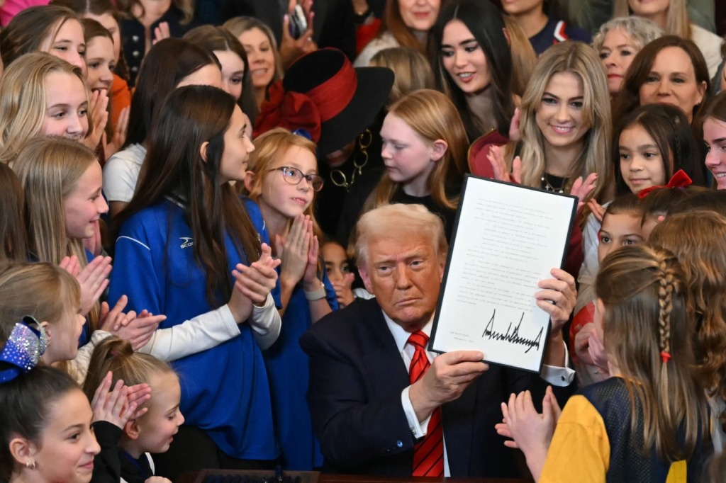 President Donald Trump signs the “Keeping Men Out of Women’s Sports” executive order at the White House as female athletes gather around the desk.