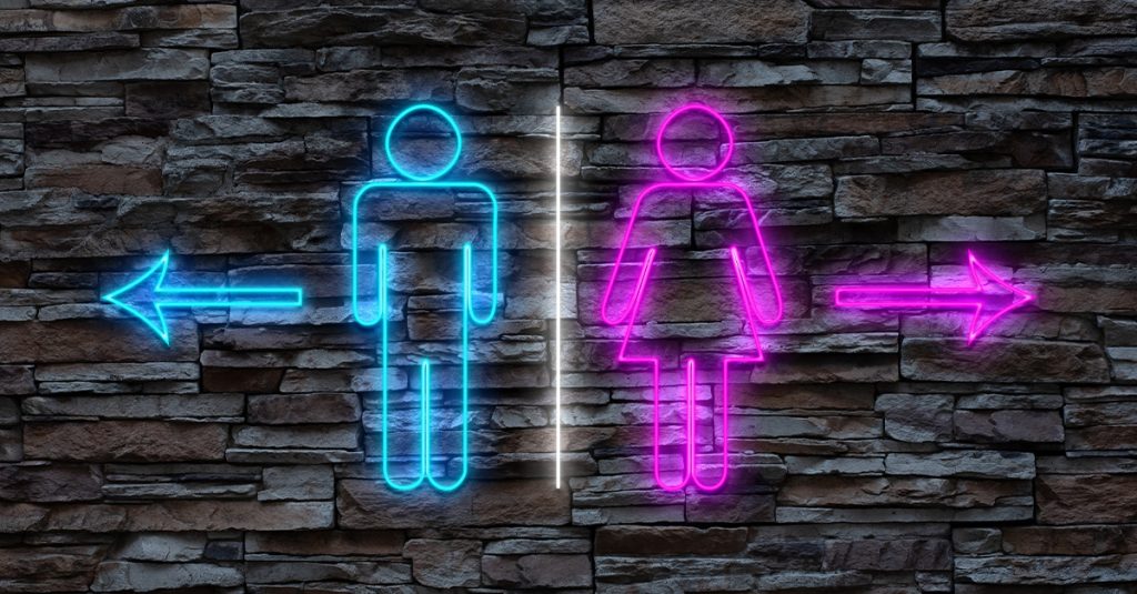A neon sign on a stone wall with signs pointing in different directions for men's and women's bathrooms.