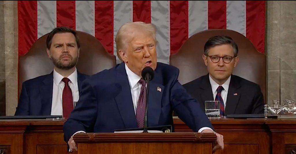 President Donald Trump speaks at a podium in the U.S. Capitol with a large American flag behind him; VP Vance and Speaker Johnson sit seated behind the dais.