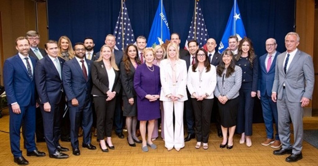 Group photo of government officials and task force members standing in front of U.S. and agency flags.