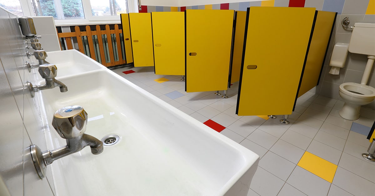Narrow school bathroom with rows of toilets and sinks
