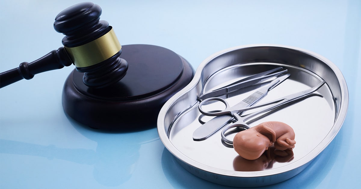 A gavel next to a tray with abortion instruments and a tiny plastic baby.