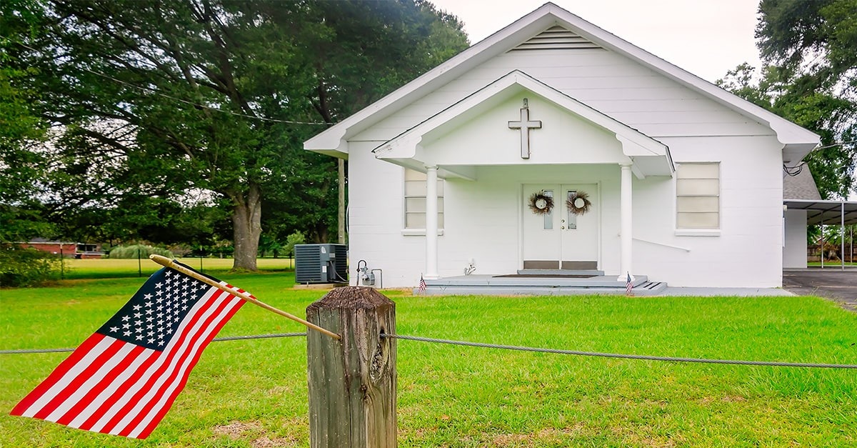 A white church bearing a cross with an American flag flying in front of it.
