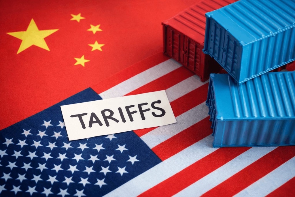 The flags of China and the United States serve as background to a photo of shipping containers and the word "Tariffs"
