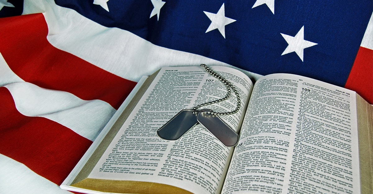 A photo of military dog tags layign on a Bible that lays on an American flag.