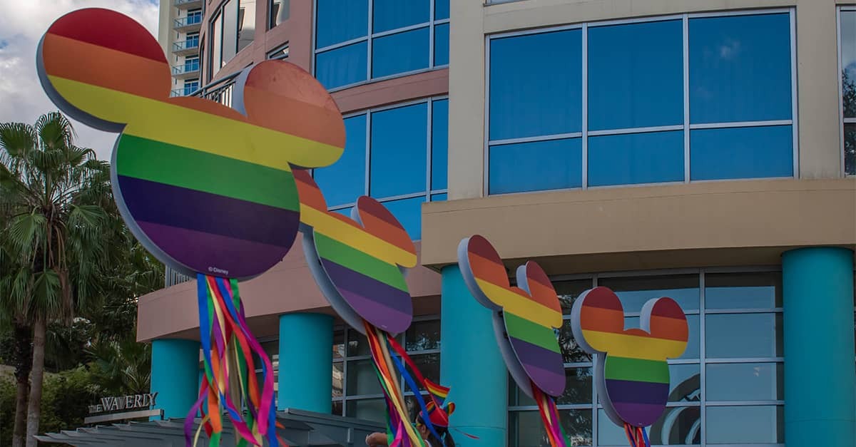 Rainbow Mickey-shaped signs with ribbon streamers outside a resort building