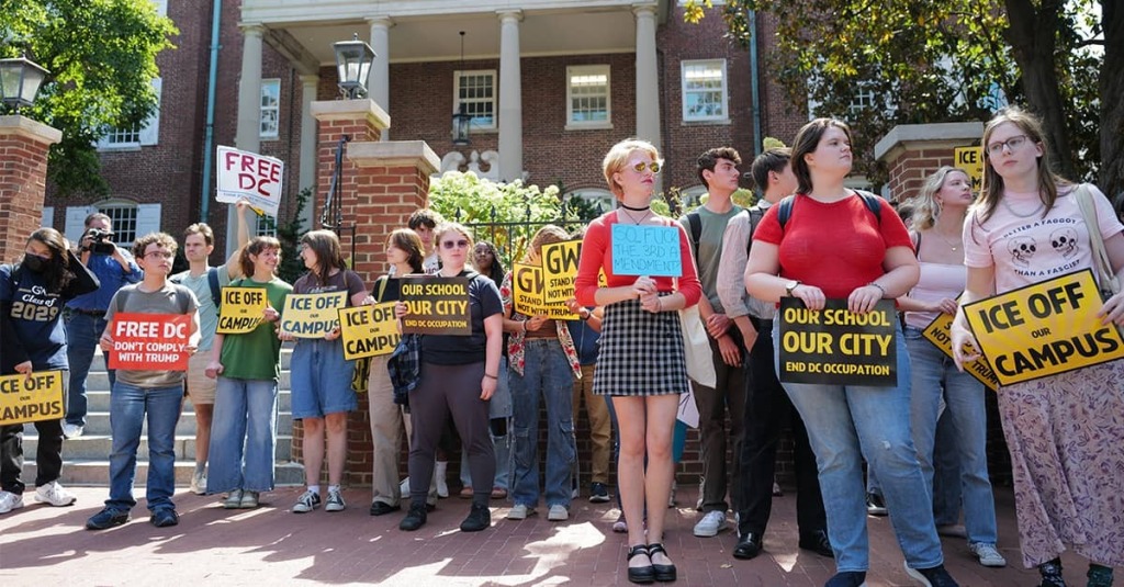 Students stand on the sidewalk out their school holding signs like "ICE Out" and "Free DC."