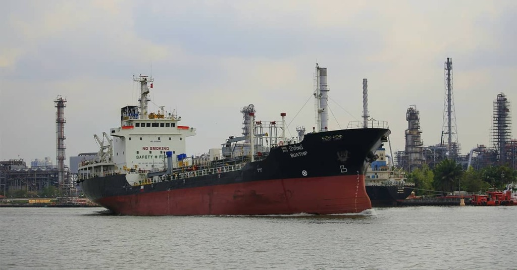 An oil tanker moves through an industrial shipping channel, highlighting the strategic importance of global energy routes like the Strait of Hormuz.