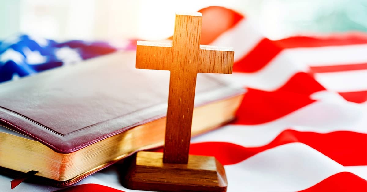 Wooden cross standing before a Bible laid over an American flag, symbolizing Christianity’s place in America’s public life and heritage.