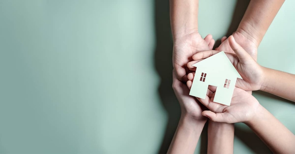 Parents and a child hold a small, wooden house model in their hands.