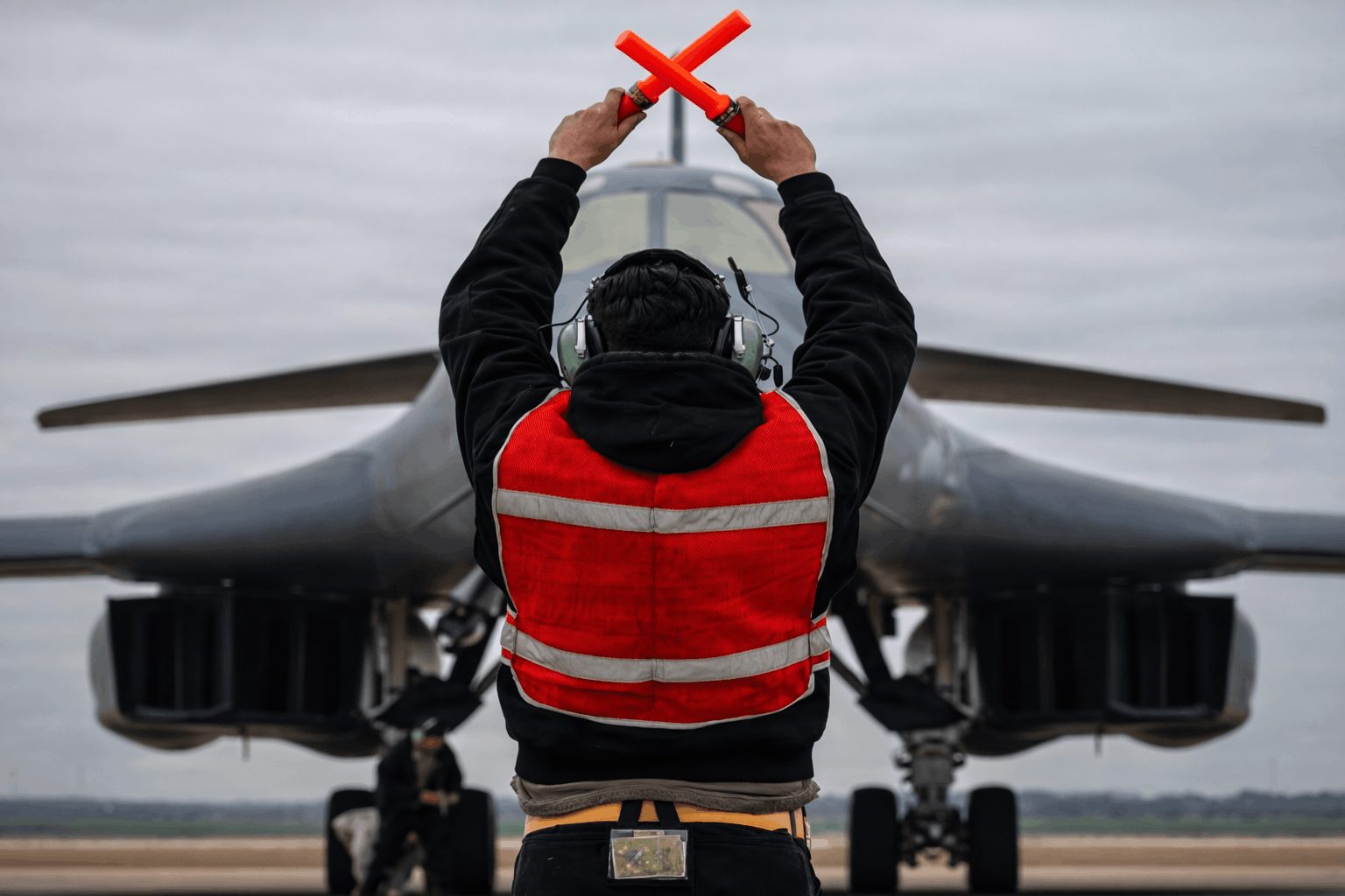A military aircraft marshaller directs a B-1 bomber on a runway in support of Operation Epic Fury.