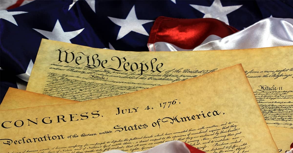A copy of the Declaration of Independence and the Constitution against the backdrop of an American flag.