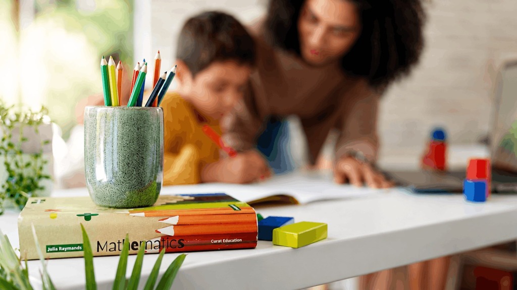 A mother seen teaching her son at the dining room table as a math book sits in the foreground.