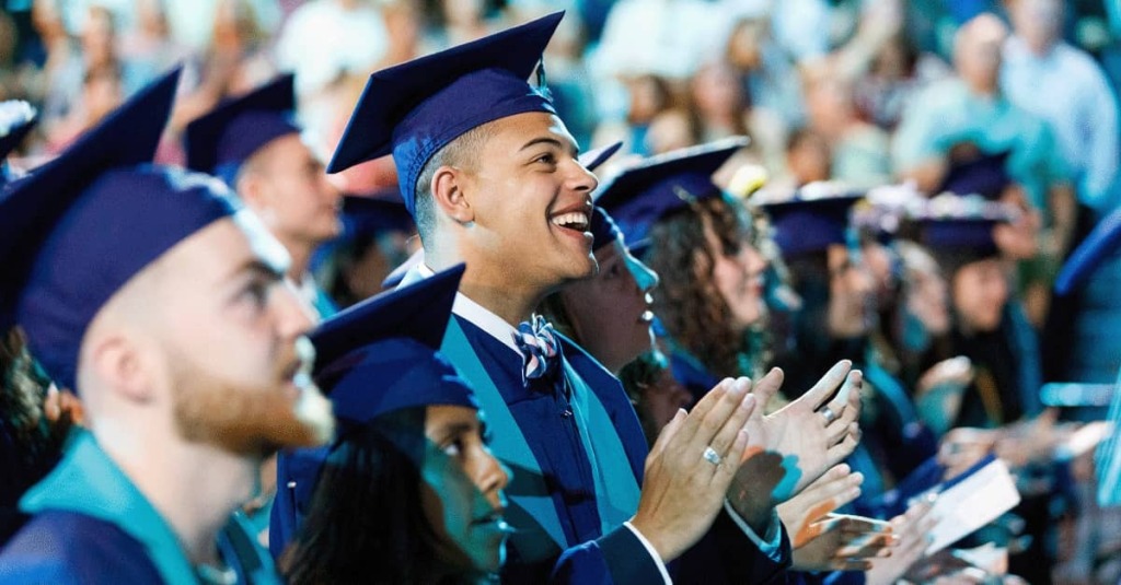 Students in cap and gowns clap during Liberty University's commencement ceremony.