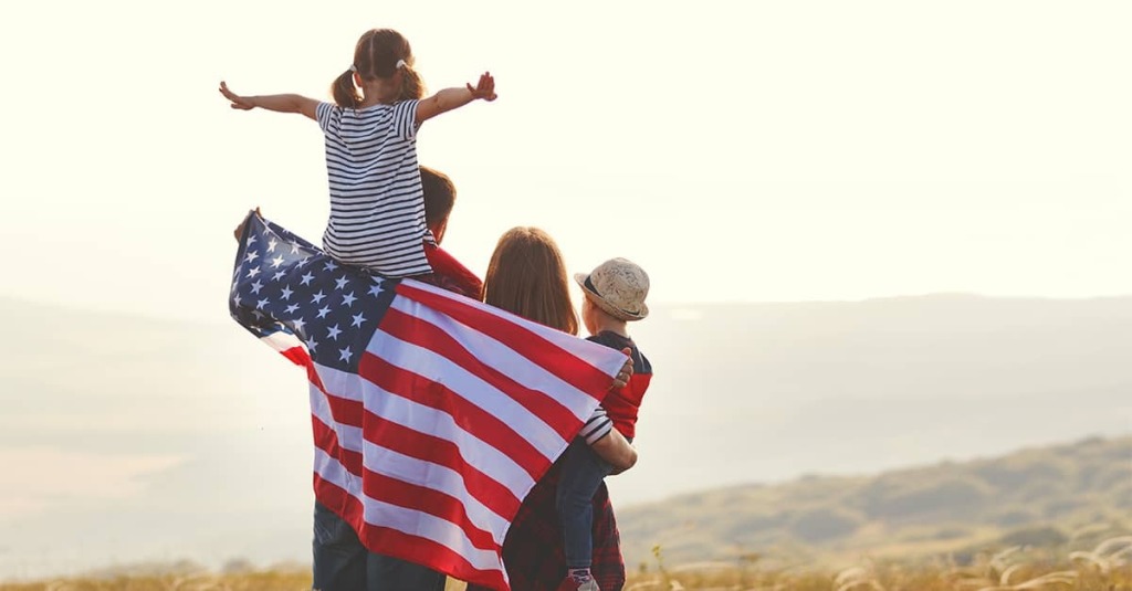 A family wrapped in the American flag looking at a sunset and praying and praising God.