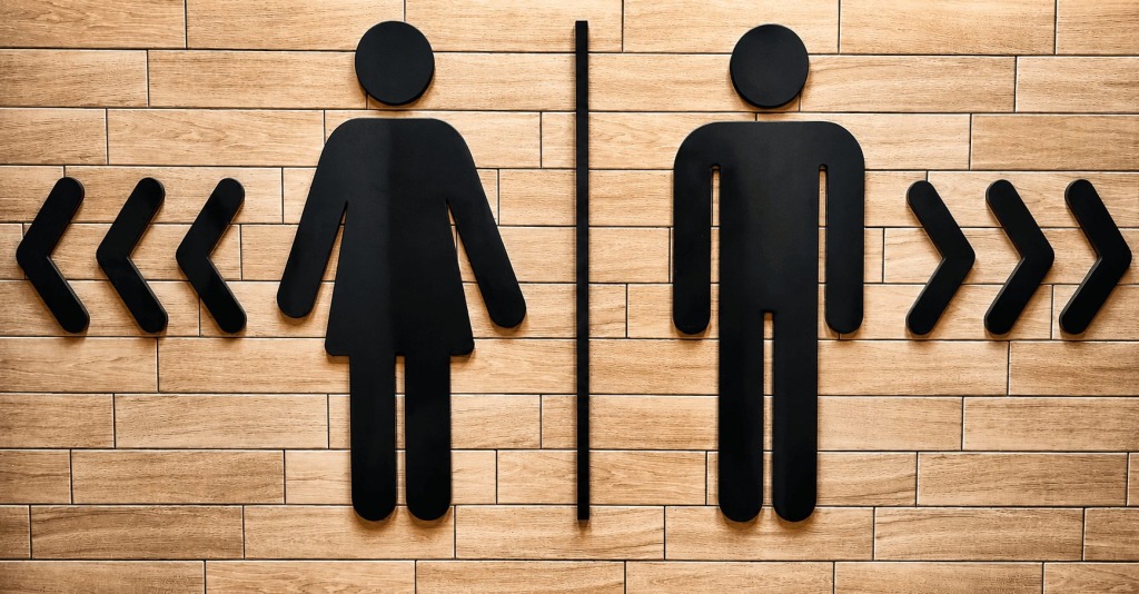 A sign showing the female symbol for the women's bathroom in one direction and the male symbol for th men's bathroom in the opposite direction.