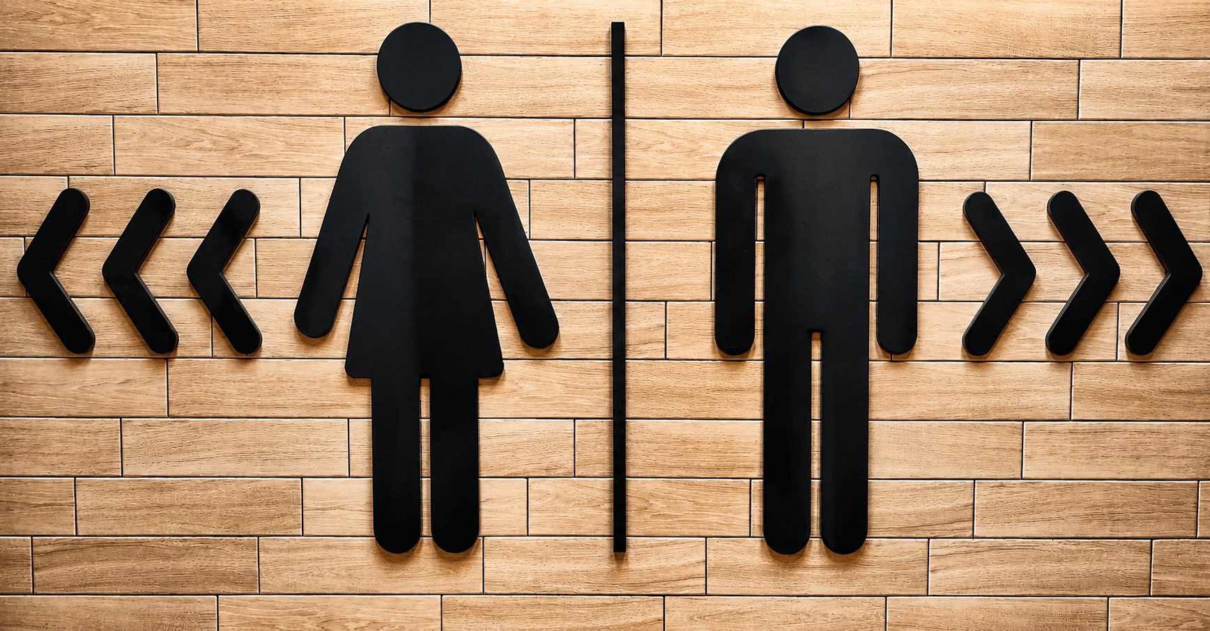 A sign showing the female symbol for the women's bathroom in one direction and the male symbol for th men's bathroom in the opposite direction.