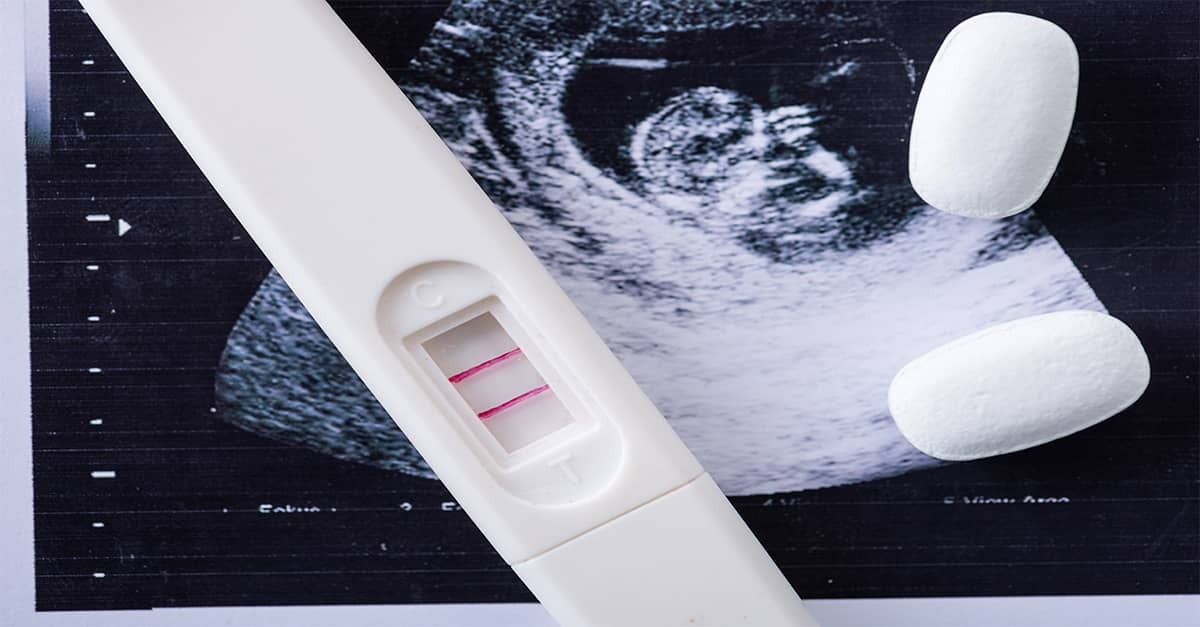 A positive pregnancy test, an ultrasound image of a 1st trimester baby and two abortion pills.