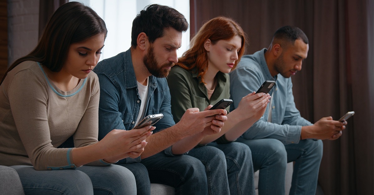A group of young people sitting next to each scrolling on their phones.