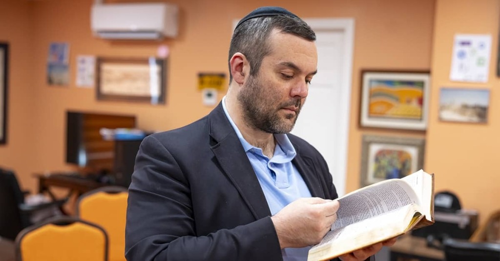 Daniel Grand, wearing a kippah, reads from a religious book in a room used for Jewish prayer and study.