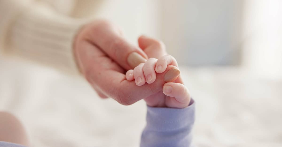 A small baby holds his mother's hand.