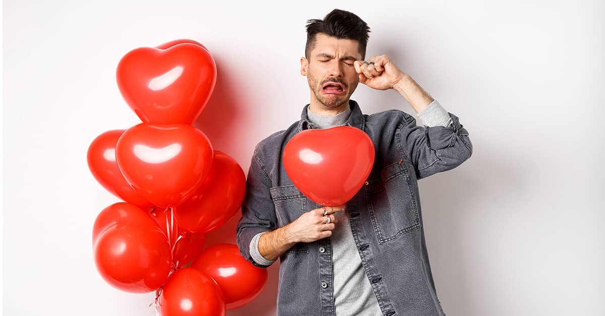 A man holding a heart-shaped balloon is seen crying.
