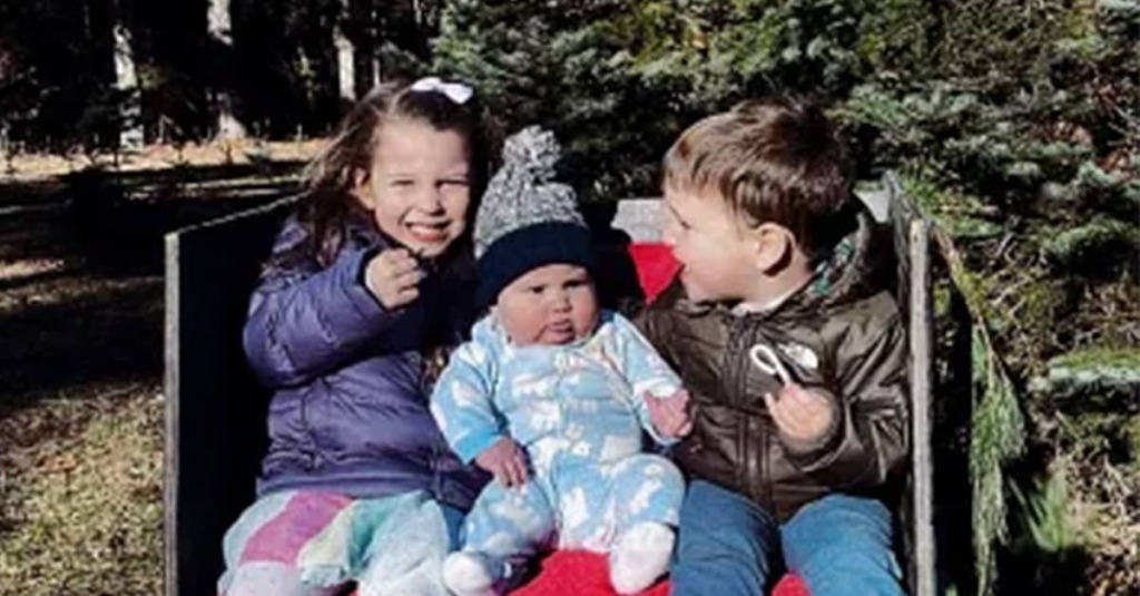 Cora, Callan, and Dawson Clancy sit on a bench at a Christmas tree farm in December 2022.