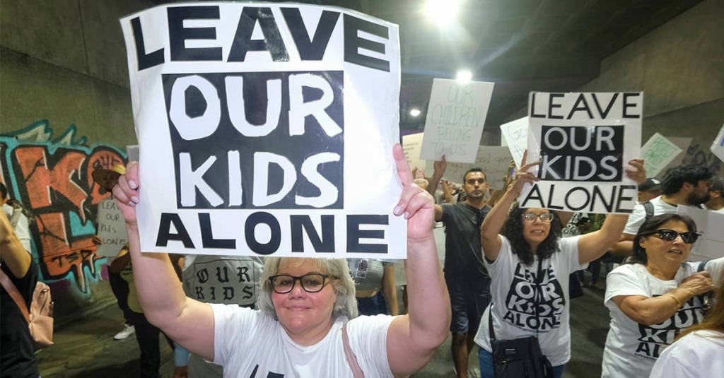 Mothers at school board hold up signs that read "Leave Our Kids Alone"