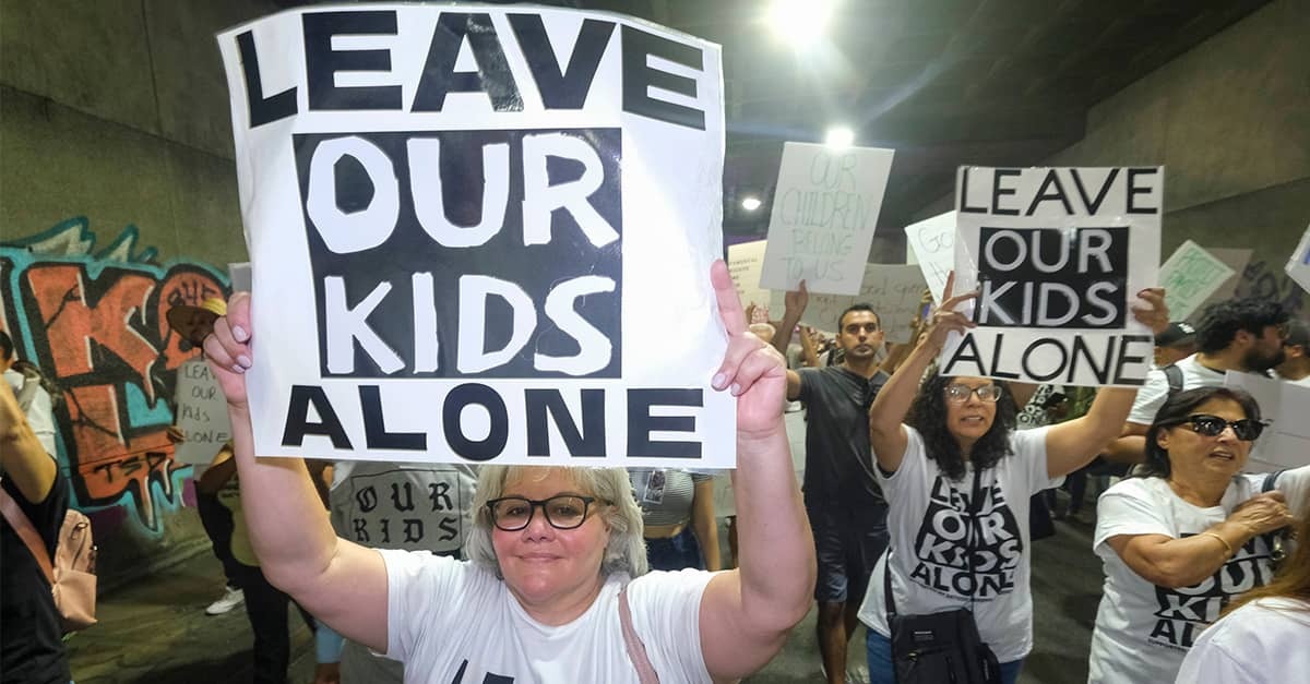 Mothers at school board hold up signs that read "Leave Our Kids Alone"